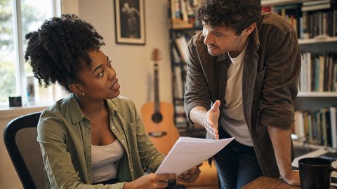 Two songwriters in a home studio setting reviewing documents in an active conversation about co-write splits