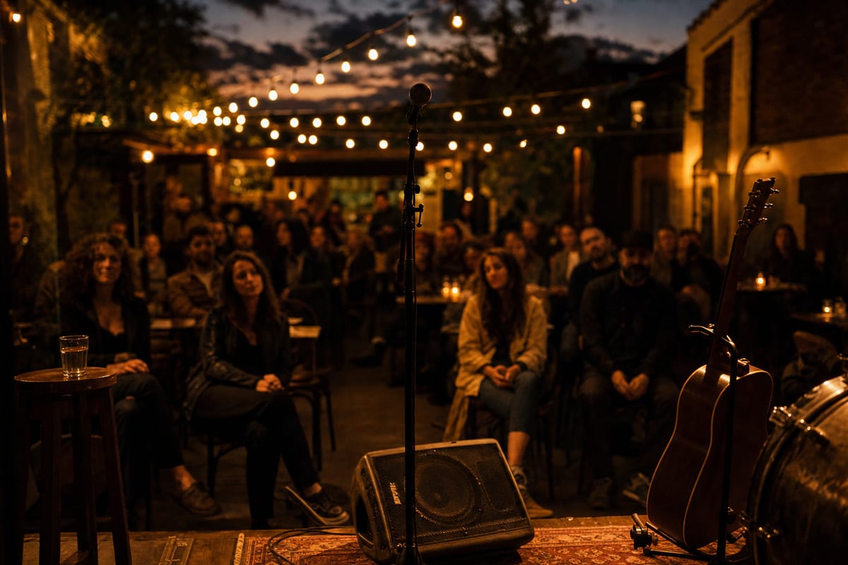 A warm editorial photo of a small live audience at an intimate venue from the performer's side of the stage at dusk, a few attentive faces in soft focus with string lights and a microphone stand in the foreground