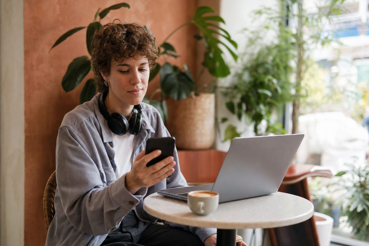 Editorial photo: a musician typing a message on a laptop with headphones and a notebook nearby, focused desk lighting, no readable text