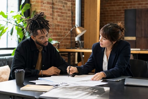Editorial photograph of an independent artist and a music industry representative reviewing documents together at a modern creative workspace with exposed brick walls, both focused on the paperwork, no logos or readable text visible.