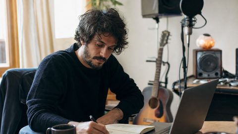 An independent artist preparing a Spotify for Artists editorial pitch with notes, headphones, and a laptop