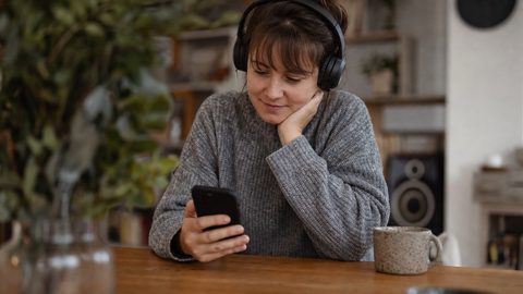 A listener viewing a personalized music playlist on a phone with headphones on a wooden table