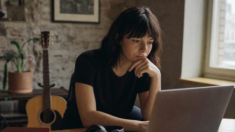 An independent musician studying listening data on a laptop in a home studio, focused and thoughtful